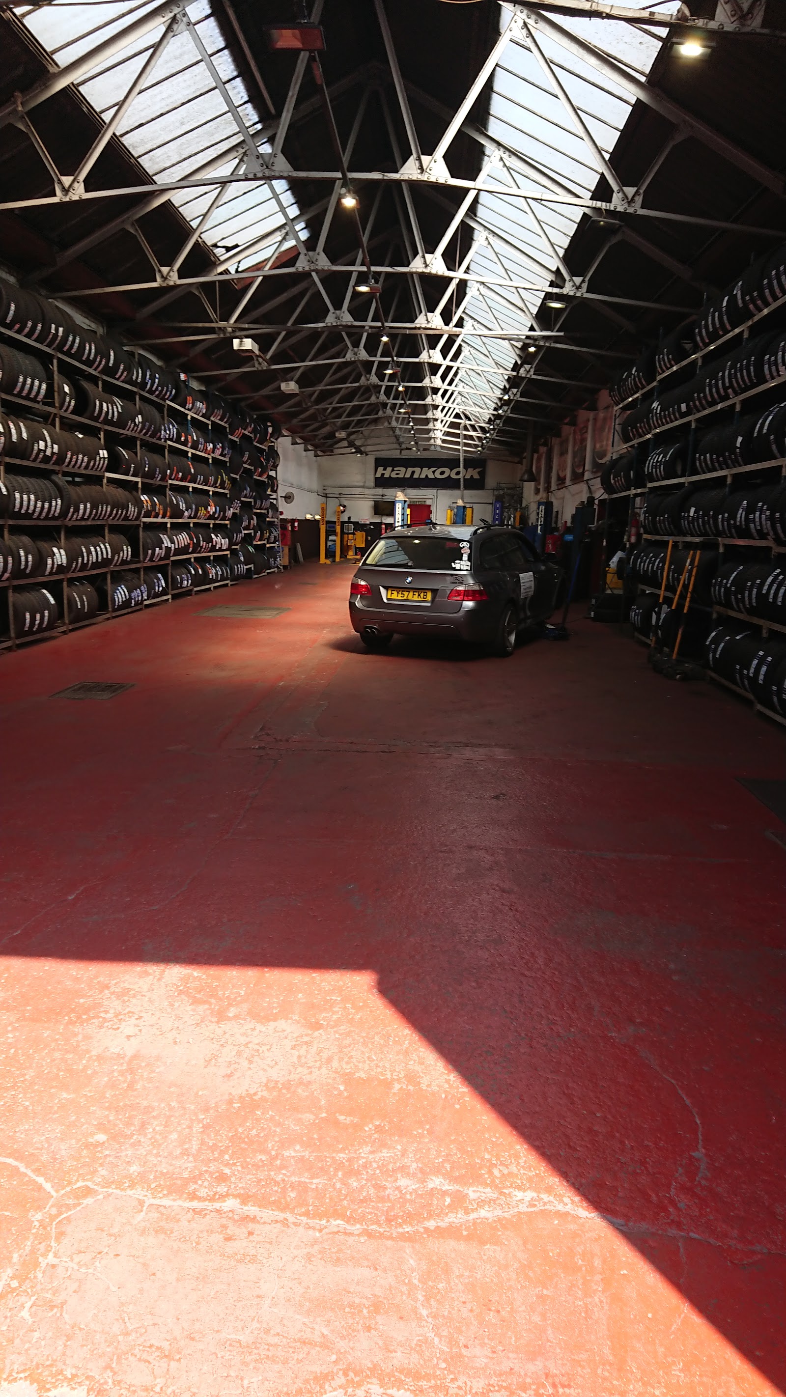 Inside the Nuneaton Exhaust Centre workshop, tyre racking and a car on the ramp
